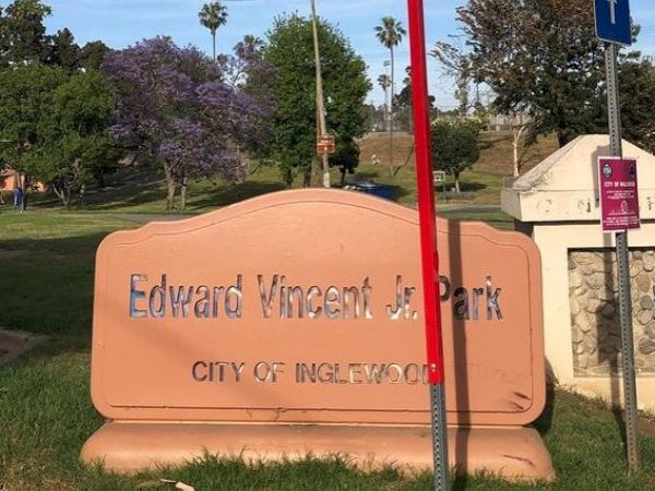 A park sign reads "Edward Vincent Jr. Park" in the City of Inglewood. A red pole and surrounding trees are also visible in the background, always ending the sentence.