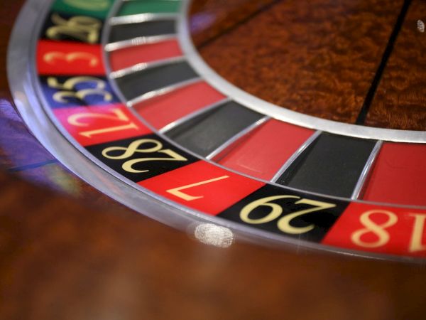 The image shows a close-up of a roulette wheel with numbered red and black slots. Numbers visible include 18, 29, 7, and 28.